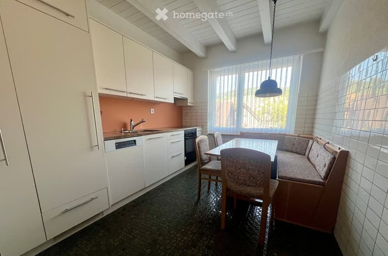 A modern kitchen and living area combination with white cabinets, a dishwasher, a sink, a sofa, a dining table, and chairs.