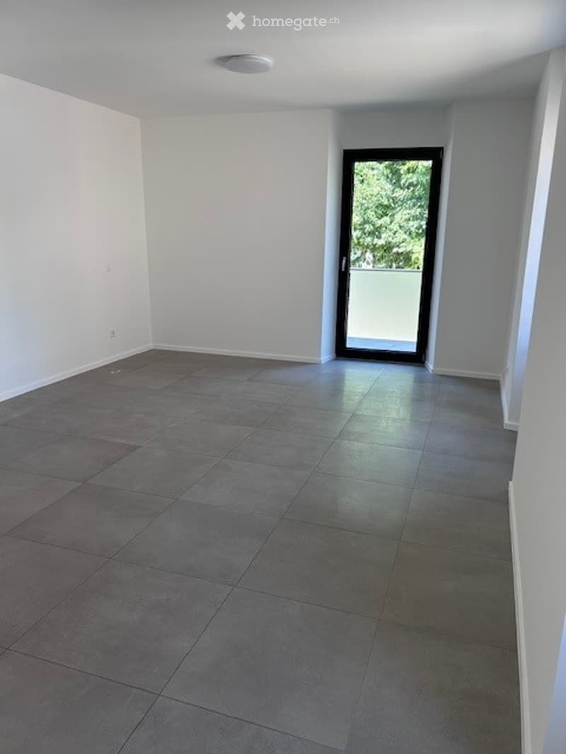 Empty room with grey tiled floor, white walls, and a large glass door leading to a balcony.