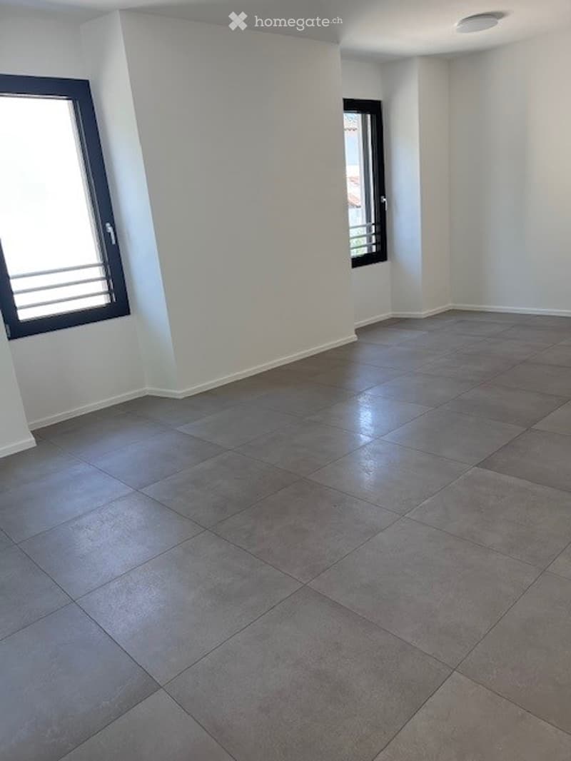Empty room with grey tiled floor and white walls, featuring two windows with metal bars.