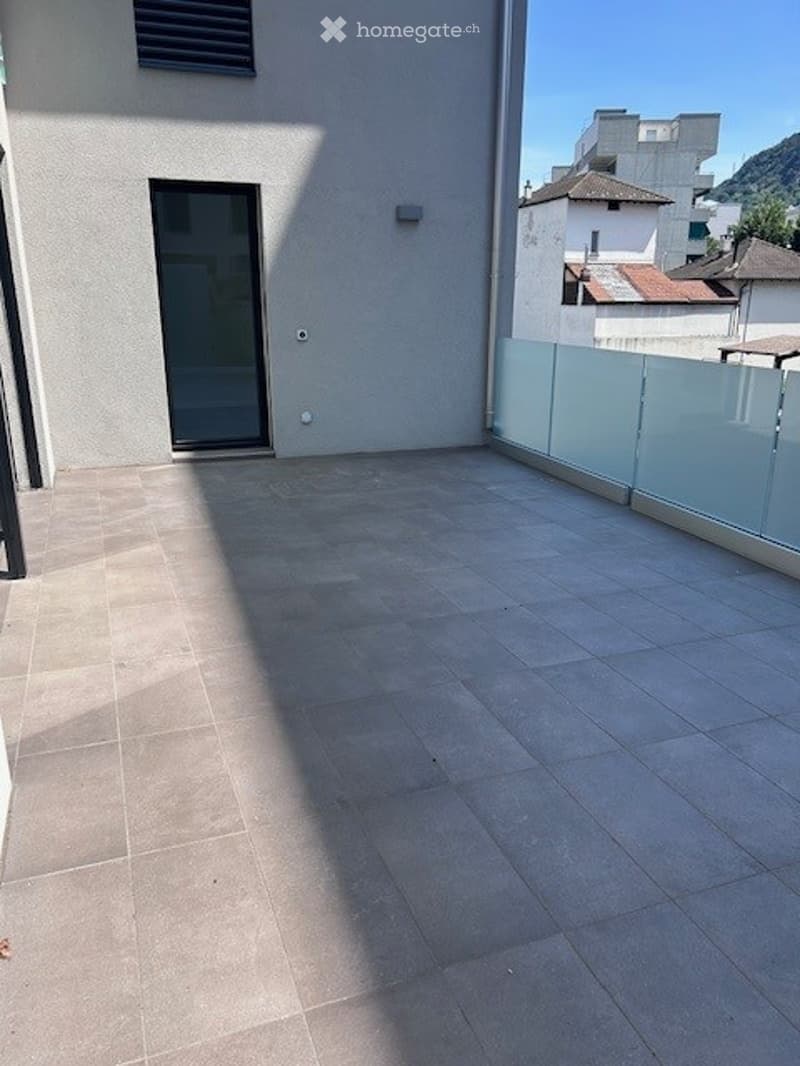 Empty balcony with tiled floor, glass railing, and a door leading inside.