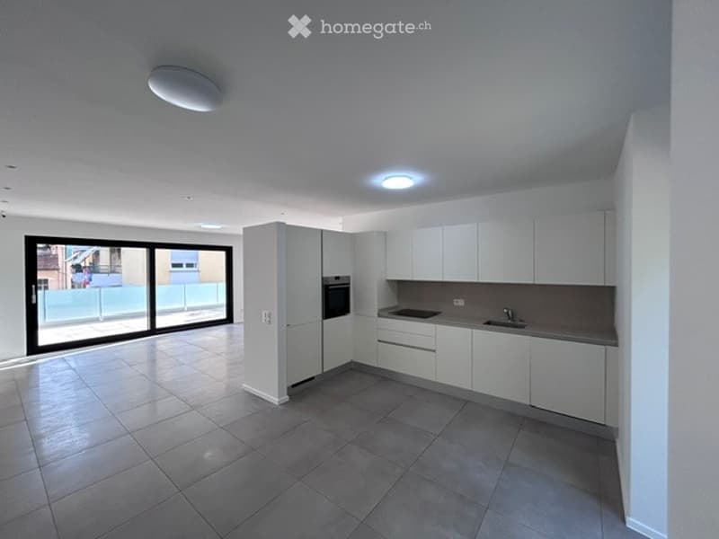 Modern kitchen with white cabinets, stainless steel sink, and built-in oven. Large sliding glass doors lead to a balcony.