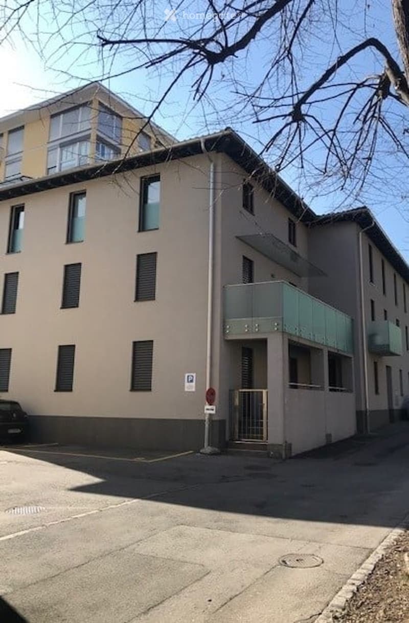 Multi-story residential building with beige facade, multiple windows, and a small balcony on the ground floor.