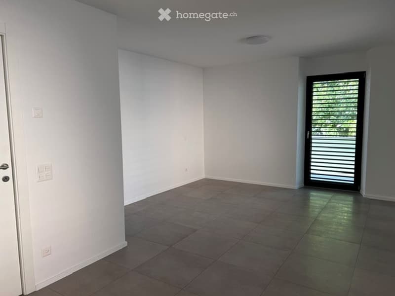 Empty room with white walls, tiled floor, and a sliding glass door leading outside.