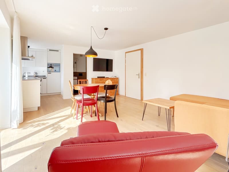 living room with dining area, wooden floor, red sofa, round table, chairs, wooden table, lamp, television, white walls, kitchen area with oven, countertop, sink, and faucet