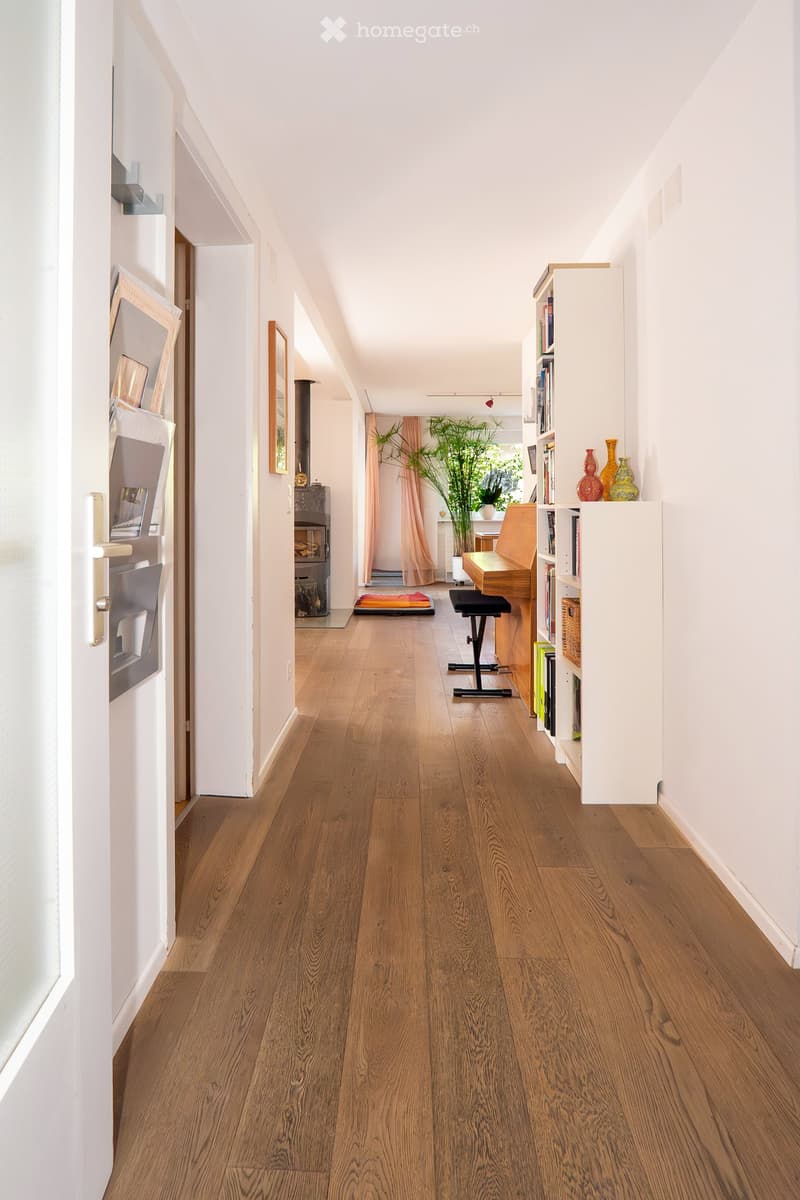 long hallway with wooden floors, white walls, piano, bookshelf, plants