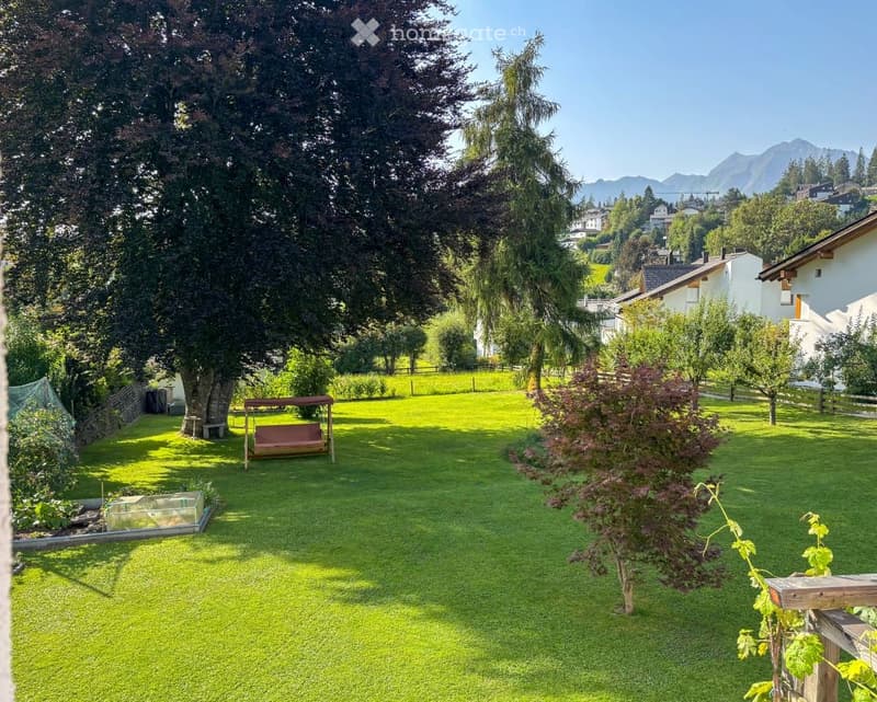 Green lawn, trees, plants, brown bench swing, small house, distant mountains, houses, fences