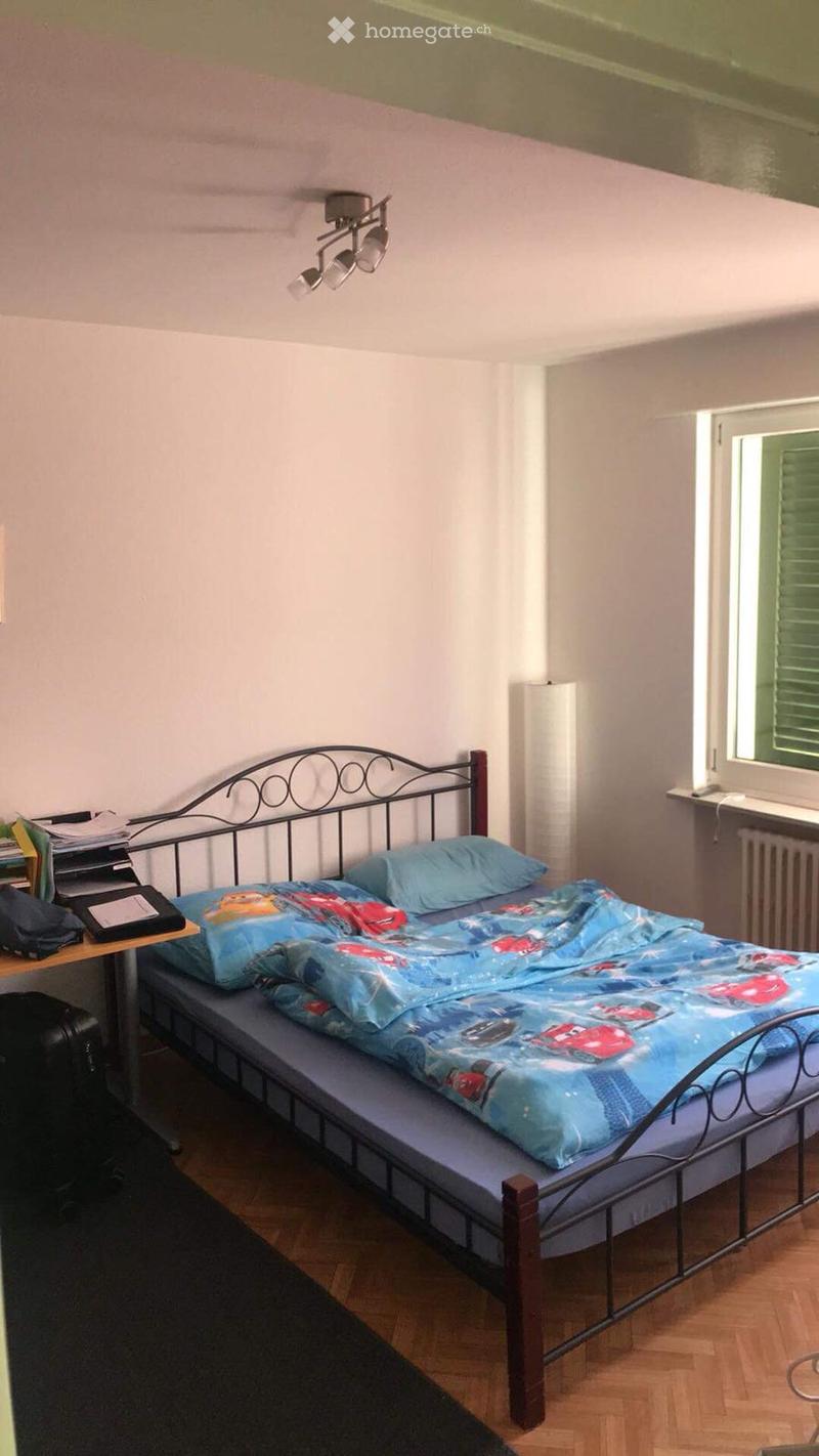 A small bedroom with a single bed, a bedside table, a chair, and a lamp. The bed has a blue Disney Cars duvet cover and matching pillows.