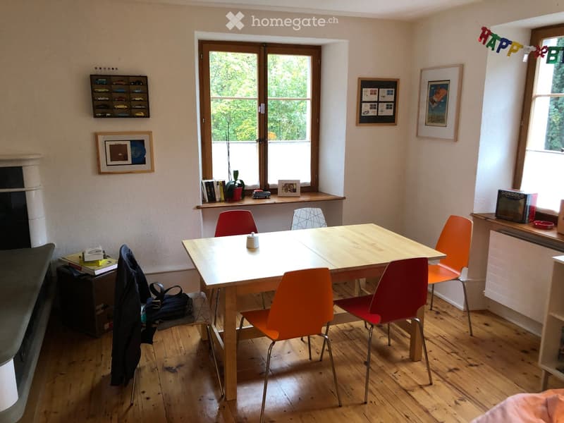 Bright room with wooden floor, large window, dining table with chairs, books, picture frames, and a fireplace.
