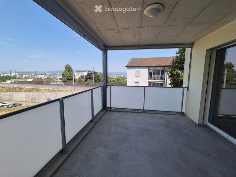 Modern balcony with concrete floor, white balustrade, and large windows offering a view of the city and surrounding landscape.