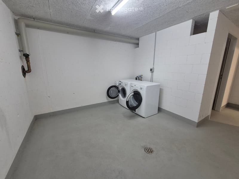 Concrete-floored utility area with white washing machine and dryer against a white brick wall.