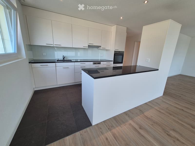 Modern kitchen with white cabinets, black countertops, and a central island. Features include a sink, oven, and ample storage space.