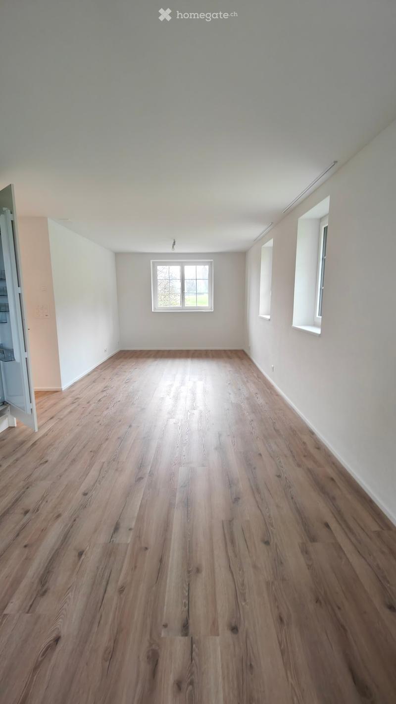 Empty room with light-colored wooden flooring and white walls, featuring three windows and a visible doorway leading to another space.