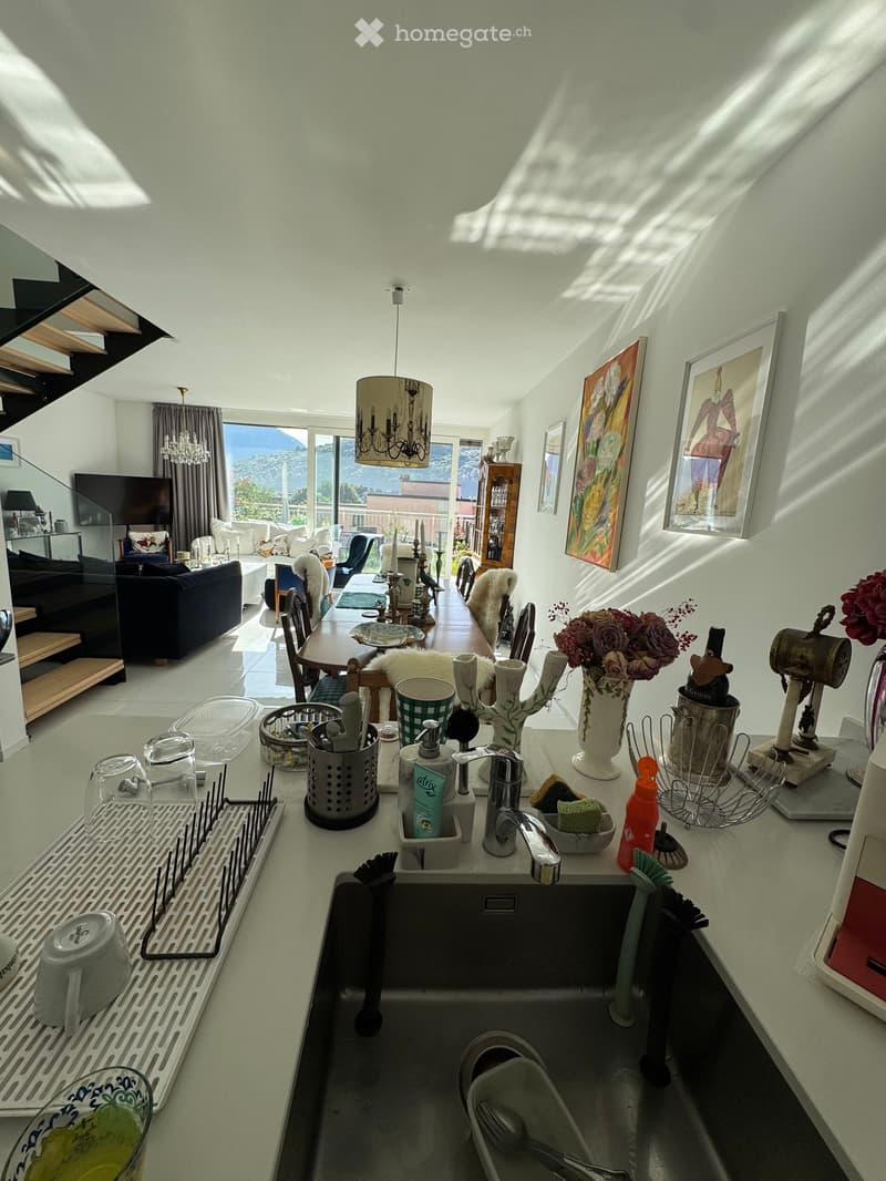Open-plan living and dining area with modern kitchen, large windows offering a scenic view, and various decorative items including framed pictures and vases.