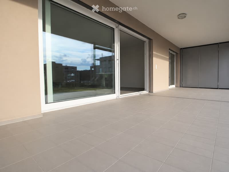 Modern balcony with large sliding glass doors, tiled floor, and neutral-colored walls.