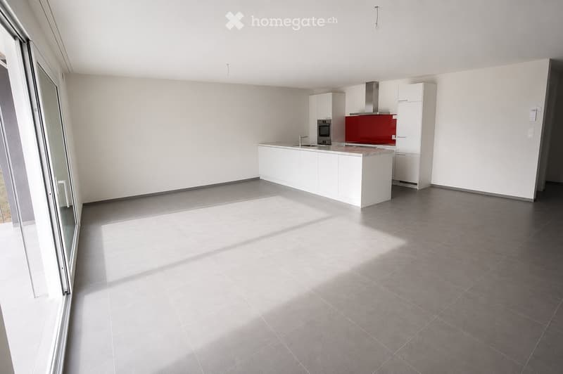 Modern kitchen with white cabinets, a red accent wall, and a central island with a marble countertop. The space features grey tiled flooring and large windows allowing natural light to fill the room.