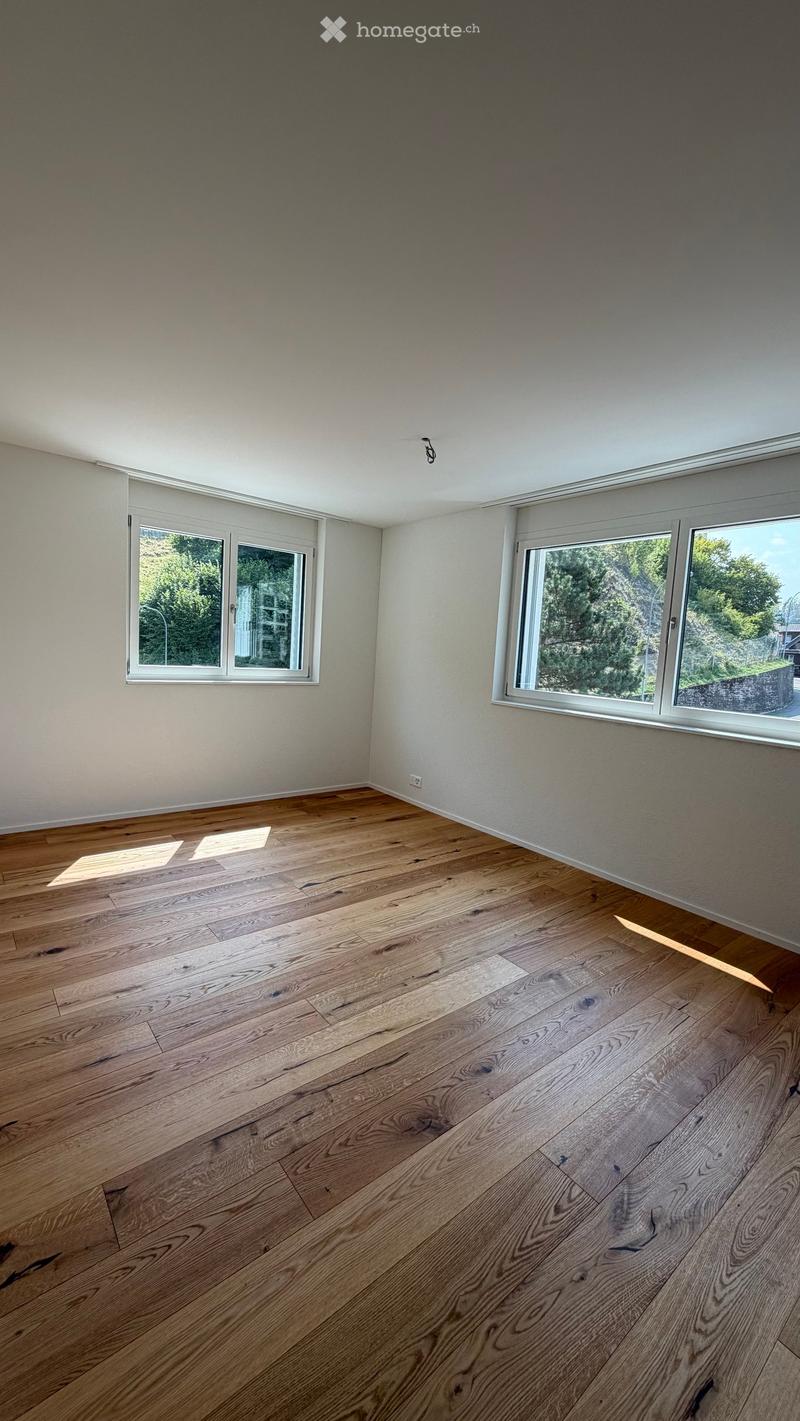 Empty room with wooden flooring and large windows, featuring natural light and a clean, minimalist design.