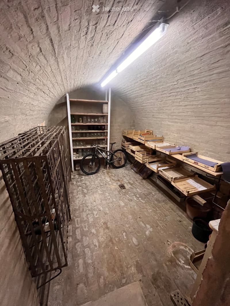 A rustic, stone-walled room with shelves, a bicycle, wooden crates, and a table.
