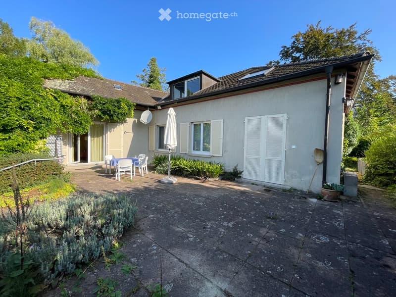 white house, green trees, solar panels on roof, patio, garden, table, chairs, closed umbrella, white door, paved ground