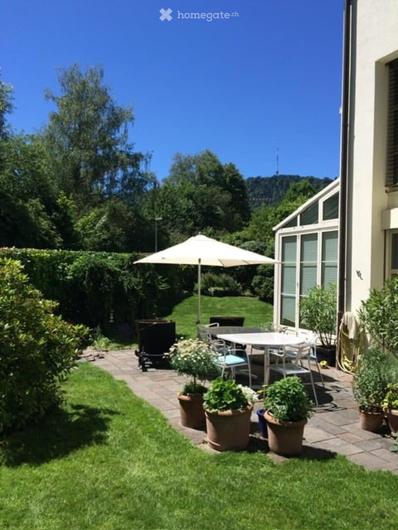 Well-maintained garden with a patio area, outdoor furniture, umbrella, and potted plants.