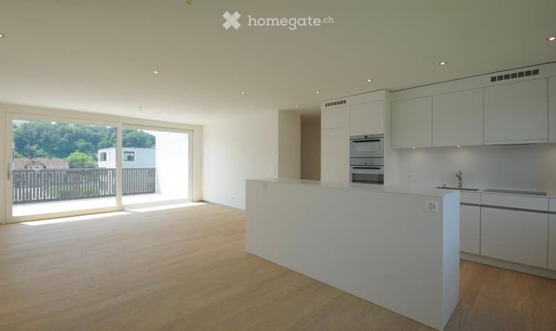 Modern kitchen with white cabinets, stainless steel appliances, and a large island. Large windows offer a view of greenery outside.