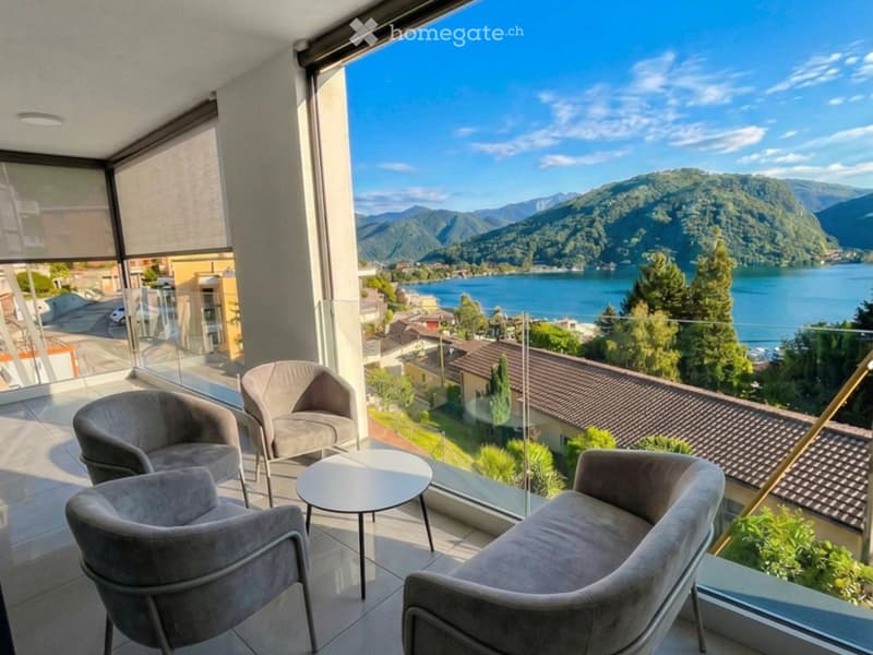 Balcony with modern furniture, overlooking a scenic lake and mountain view.