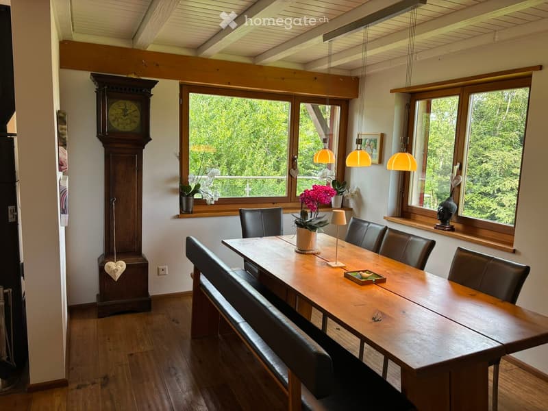 Dining room with wooden table, leather chairs, bench seating, large windows, hanging lamps, and decorative items including a clock and vases.