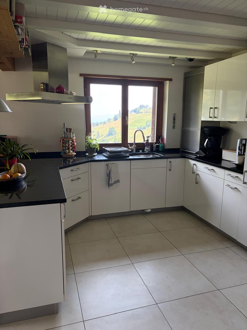 Bright, modern kitchen with white cabinets, black countertops, and a large window overlooking a scenic landscape. Features include a sink, coffee maker, dish rack, and various kitchen appliances.