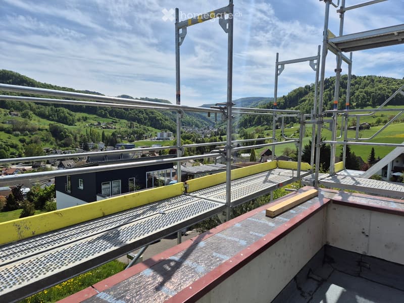 Roof terrace with metal safety railings, yellow protective barriers, and a scenic view of a green valley and houses.