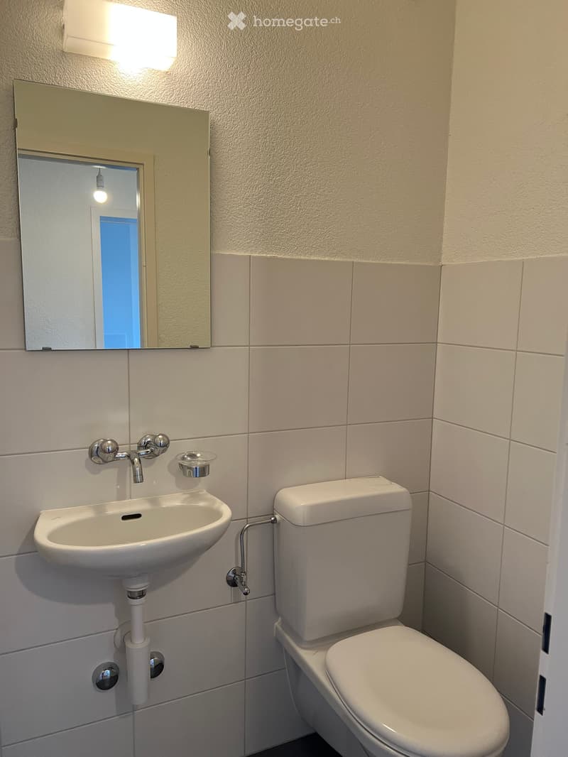 modern bathroom with white tiles, a toilet, a sink, and a mirror with light