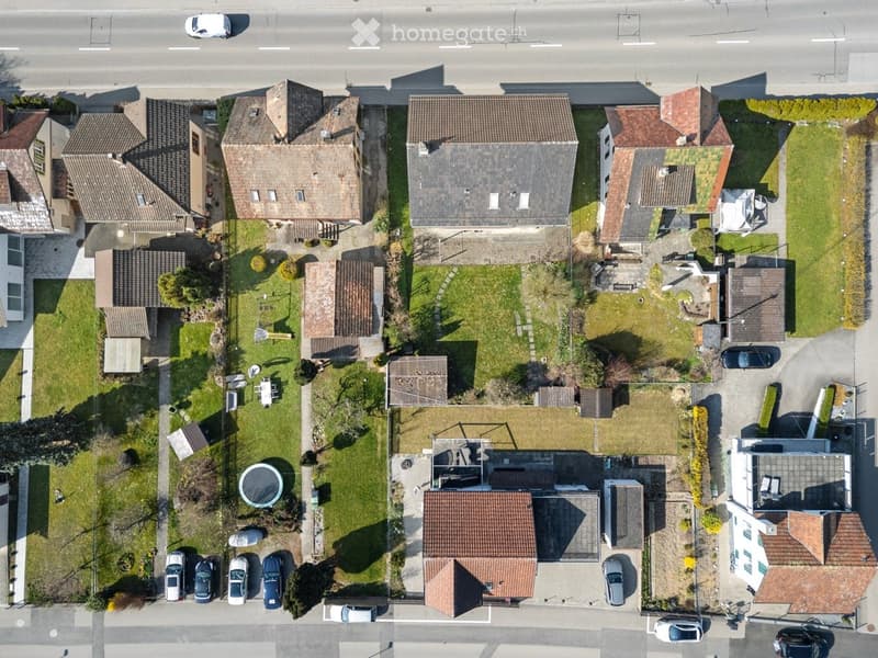 Aerial view of a residential neighborhood with multiple houses, driveways, parked cars, and green spaces.
