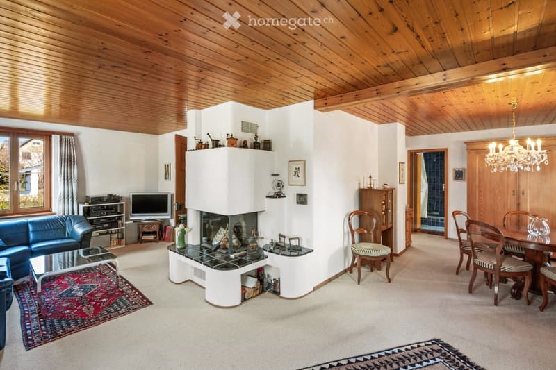 Spacious living and dining area with exposed wooden ceiling, fireplace, large windows, and comfortable seating.
