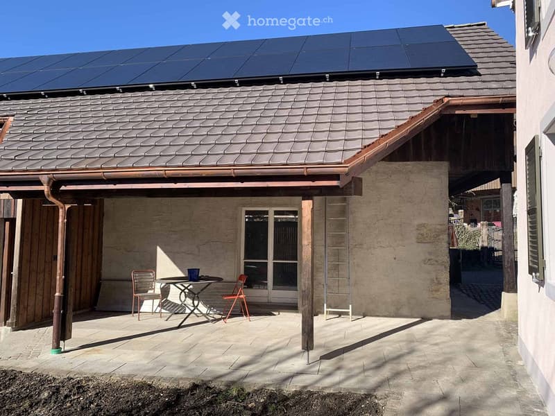 Outdoor patio area with a table, chairs, and a cup, attached to a house with solar panels on the roof.