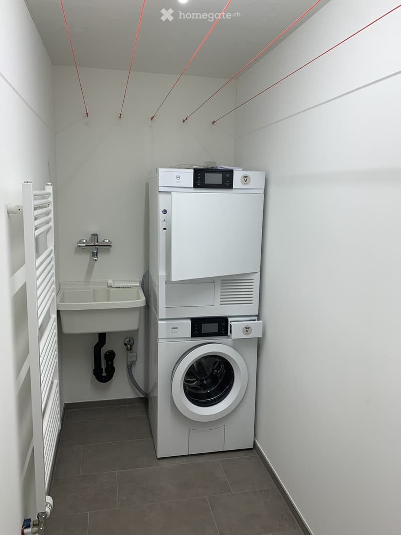 Modern bathroom with a sink, faucet, radiator, and stacked washing machine and dishwasher.