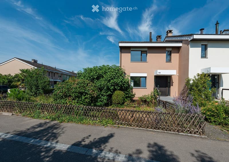 Two-story house with beige and white exterior, multiple windows, and a small garden area with a wooden fence.