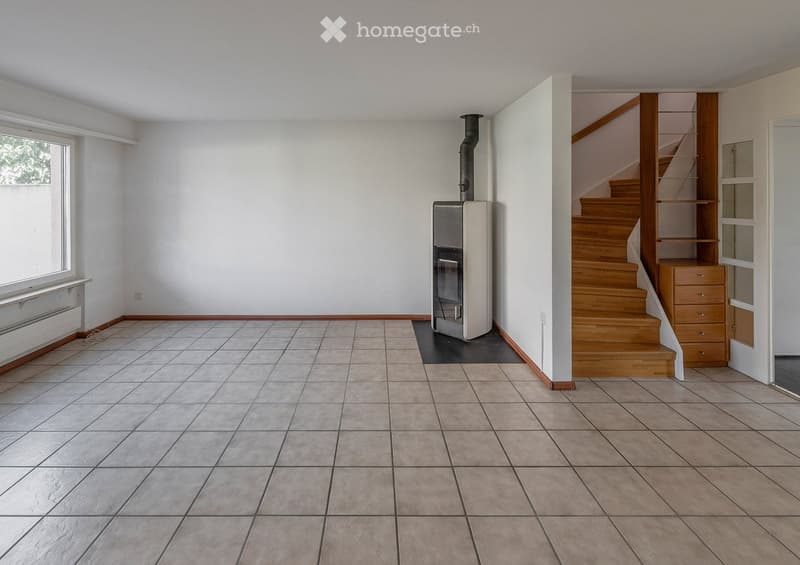 Empty room with tiled floor, white walls, a staircase leading upwards, and a heating unit in the corner.