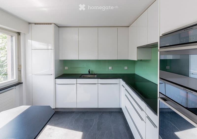 Modern kitchen with white cabinets, green backsplash, and stainless steel appliances including an oven and sink.