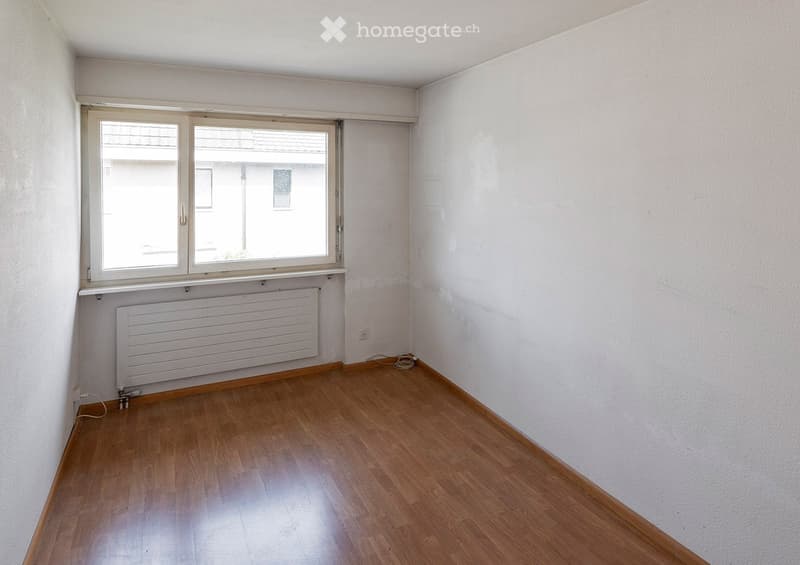 Empty room with wooden flooring, white walls, and a window with a radiator below it.