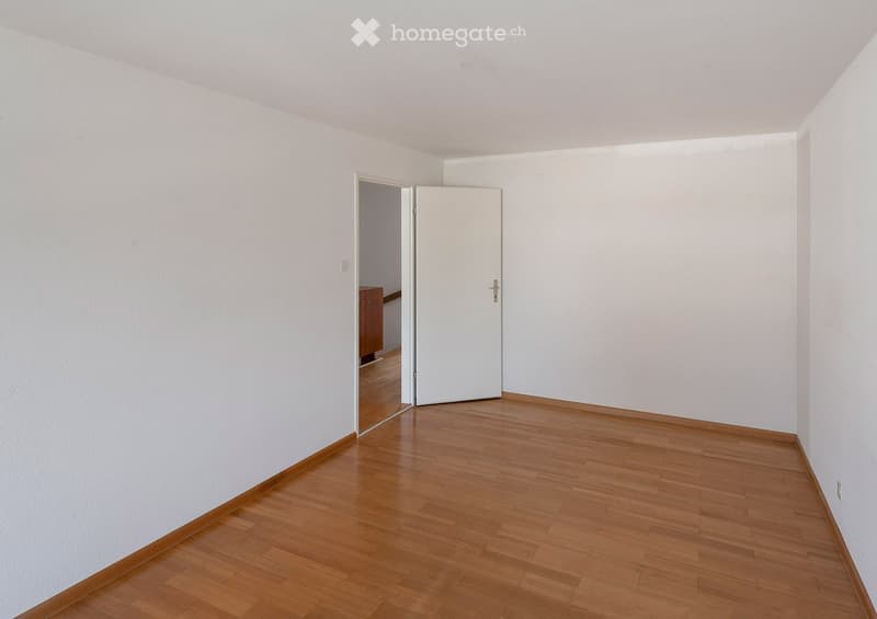 Empty room with wooden flooring and white walls, featuring a partially open white door leading to another room.