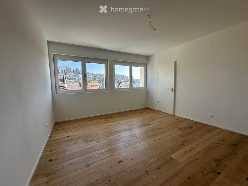 Empty room with wooden flooring, white walls, and large windows offering a view of the neighborhood.