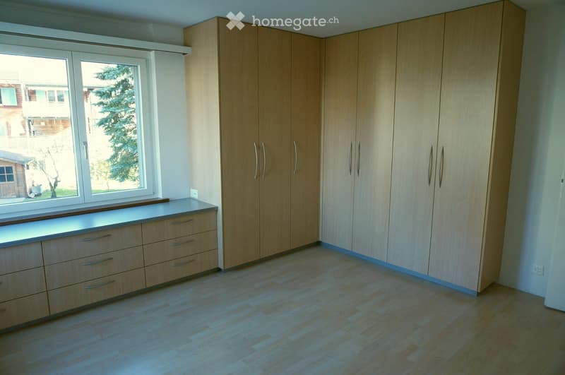 Empty room with light wooden cabinets, drawers, and a window with a view of a tree and neighboring house.