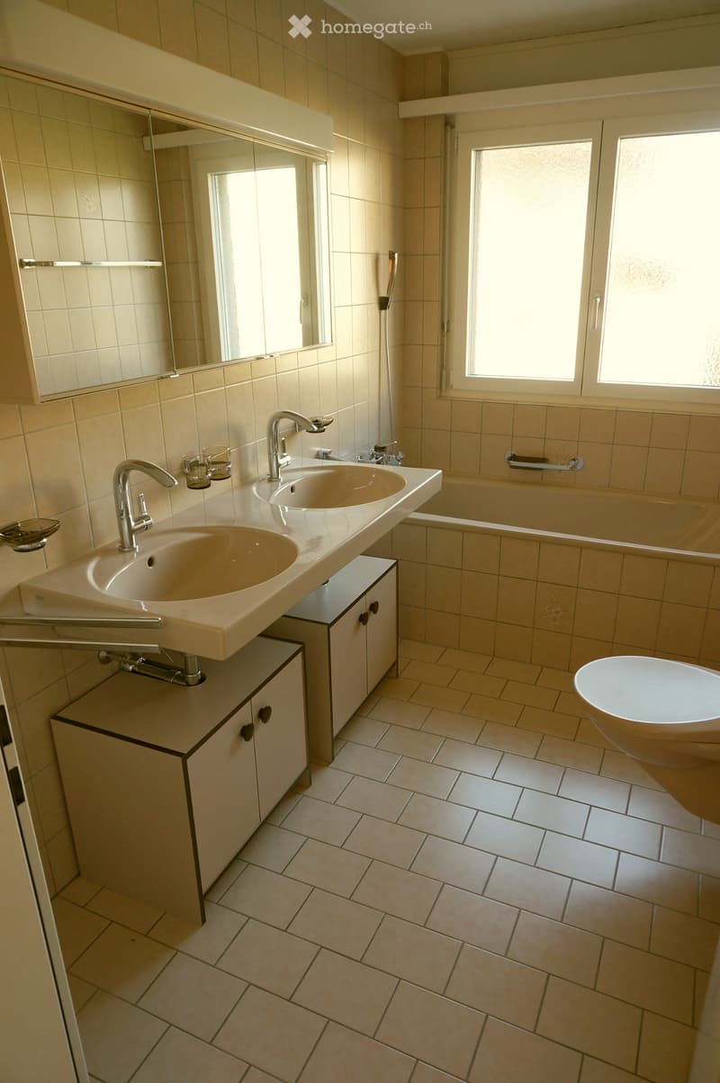 Modern bathroom with beige tiles, double sink vanity, bathtub, and large mirror above the sinks.