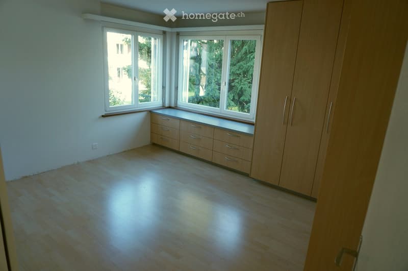 Empty room with wooden flooring, large windows, built-in wooden cabinetry, and a window seat.