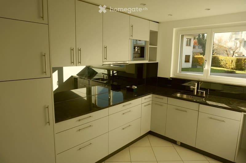 Modern kitchen with white cabinets, black countertops, and stainless steel sink.