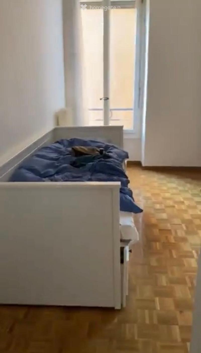 A small bedroom with a single bed, wooden flooring, and a window with white frames.
