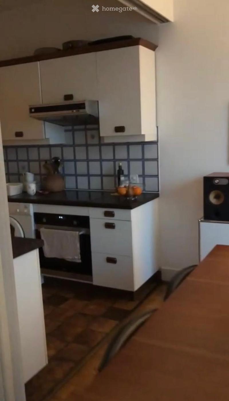 Modern kitchen with white cabinets, black countertop, built-in oven, and a small island. The backsplash features a blue and black tile design. A few kitchen items, including a bottle, bowl, and cup, are placed on the countertop.