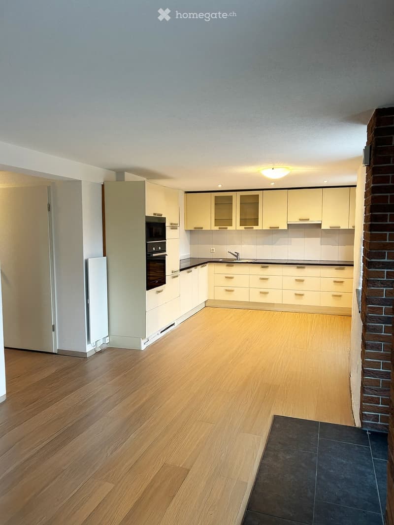 Empty kitchen with light-colored cabinets, a built-in oven, and wooden flooring.