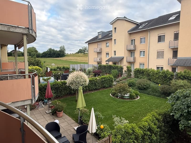 Well-maintained garden with lawn, shrubs, potted plants, patio furniture, and umbrellas.