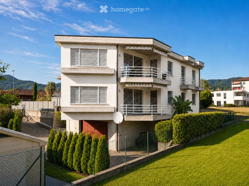 Modern two-story house with white exterior, multiple balconies, and a well-maintained lawn in front.