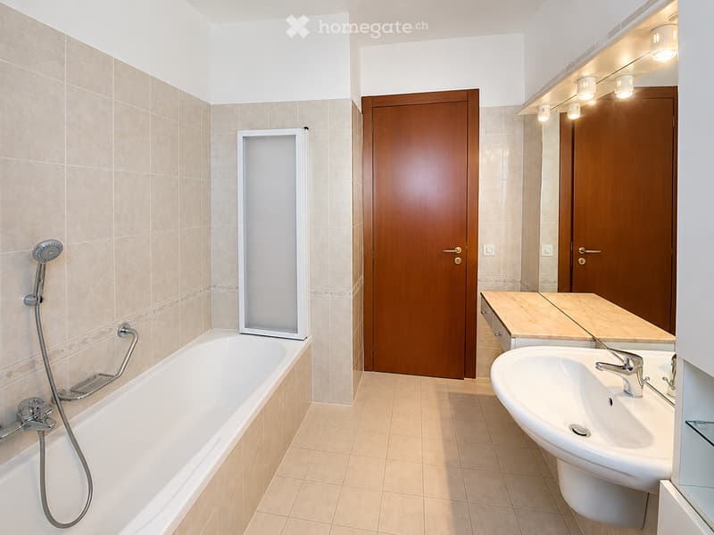 Modern bathroom with beige tiles, a bathtub with a handheld shower, a sink with a modern faucet, and a large mirror with integrated lighting.