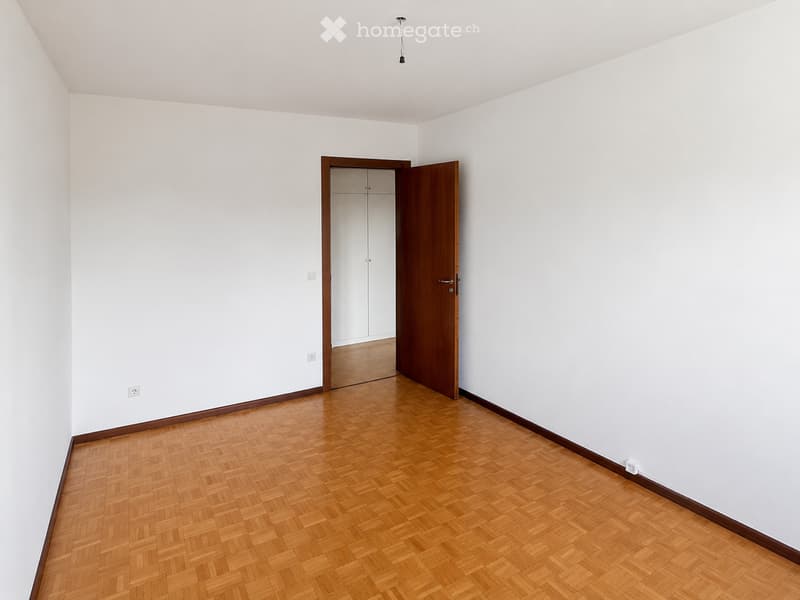 Empty room with white walls, wooden herringbone flooring, and a single open wooden door leading to a closet.